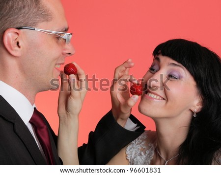 Happy smiling bride and groom young happy couple playfully eating strawbery on red background