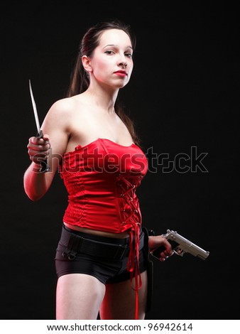 Sexy young woman in red with a gun and knife on black background