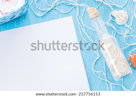 Glass bottle with sand, white blank paper, and knitted fishing net on blue scratched desk