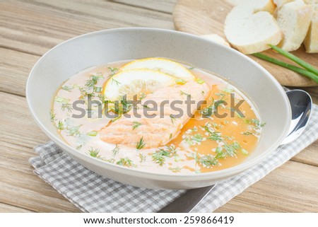 Salmon soup sprinkled with dill, served with green olives and lemons on wooden desk background