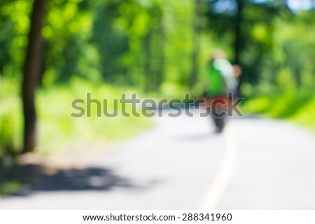Couple driving scooter through the green wood. Lifestyle image with blur effect.