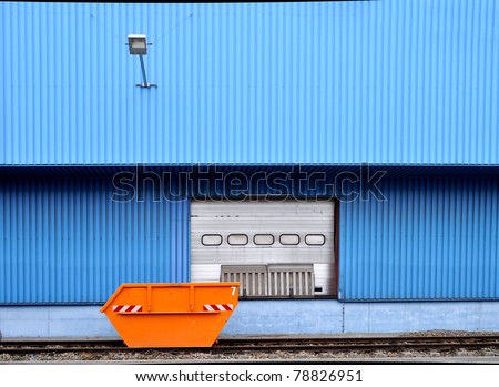 Orange waste container in front of a factory building with blue cladding