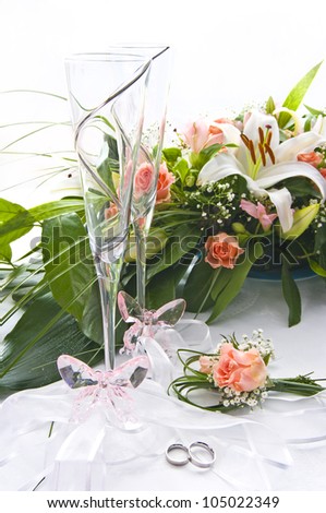 White table with wedding decoration of flower bouquet, glasses, crystal butterfly and wedding rings in front.