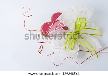 Heart-shaped biscuits decorated with inscription for Valentine\'s Day and a fancy white and green bow, and red swirls.