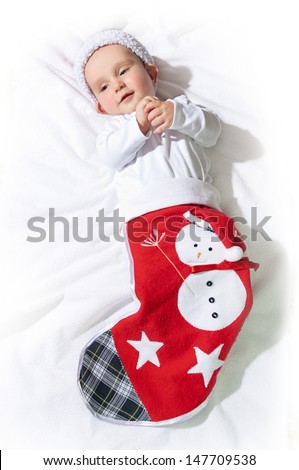 Cute funny baby in a Christmas handmade sock lying on a fluffy white background