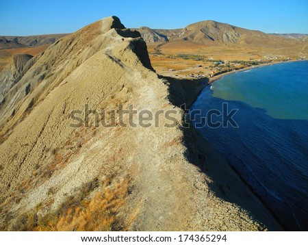 Photo. Sandy Cape, sea shore. Sunny day, the summer heat. Sea beach, blue sky. Path, path. Seaside resort. Bright light and contrast shadow of mountains.
