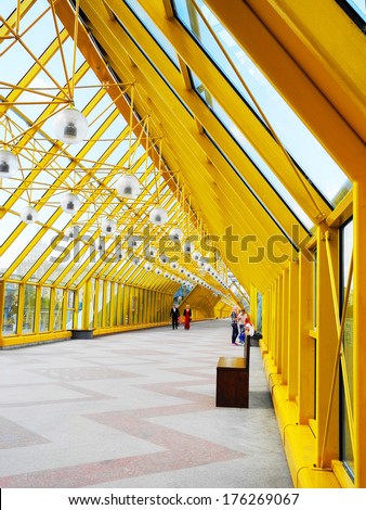 Yellow bridge of trusses and beams. Indoor glass bridge for pedestrians. Sunny day, bright light and contrasting shadows.