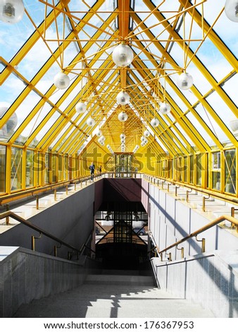 Yellow bridge of trusses and beams. Indoor glass bridge for pedestrians. Sunny day, bright light and contrasting shadows. Path, road, lights
