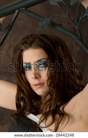 A sultry young woman poses against an iron bed frame