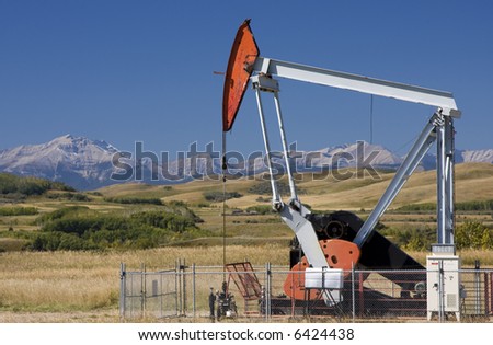 An oil well pump in the foothills of Alberta with the Rocky Mountains in the background.