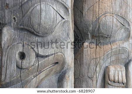 Detail of two faces on a pair of old, worn, unpainted, wooden West Coast Indian totem poles in a Vancouver, British Columbia park.