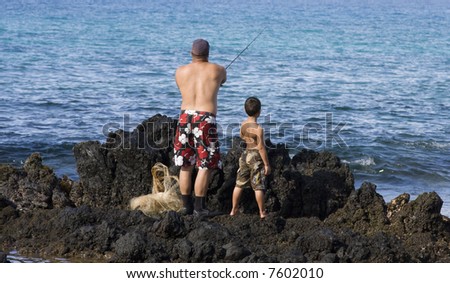 On an outcrop of lava rock in Hawaii, a father shows his son how to cast a fishing rod.