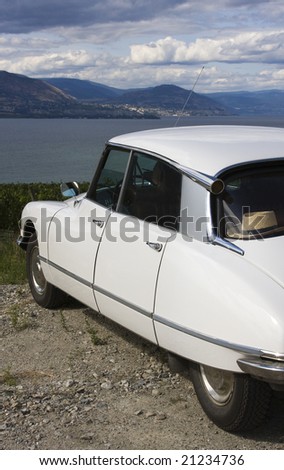 A classic, streamlined, white French car is parked overlooking a lake.