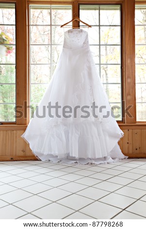 stock photo Beautiful White Wedding Gown Hanging by Window