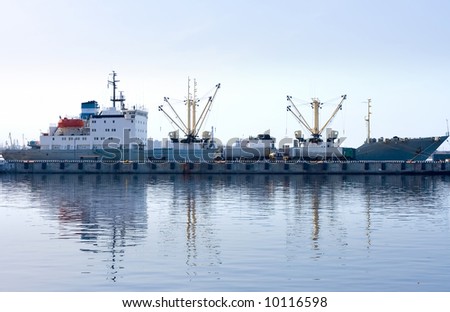 cargo ship docked and loading in port fully reflected in water