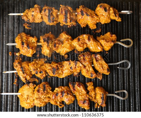 Indian lamb tikka kebabs cooking on hot griddle plate.
