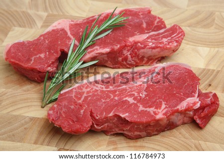 Fresh raw sirloin beef steaks on butcher\'s block chopping board.