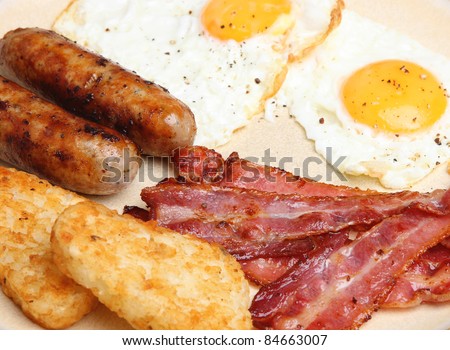 Cooked breakfast with fried eggs, sausages, bacon and hash browns.