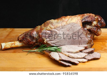 Roast leg of lamb on wooden carving board. Visible steam rising.