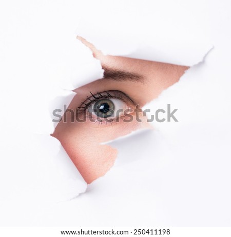 Women  eyes through a hole in a paper