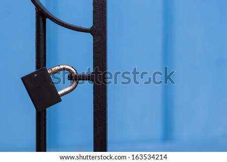 A padlock on a black gate in front of a blue background.