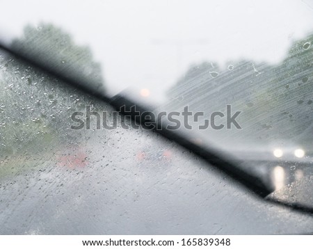 A windscreen wiper moving across a windscreen whilst a car drives on a very wet day.