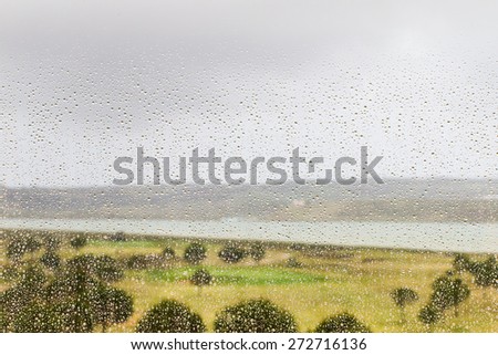 Rain drops covering a window during a storm with a view of the Guadiana RIver in Southern Spain and a golf course behind the window.