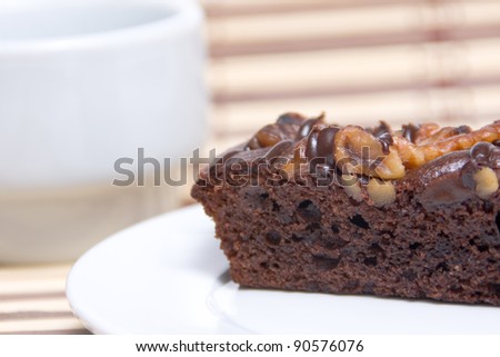 Closeup of a piece of chocolate cake with nuts on a plate with a cup of background