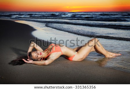 beautiful young slim girl lying down on sand at the water