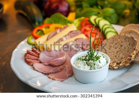 Small bowl of cottage cheese on a plate with slices of home-smoked tenderloin, cheese, smoked ham, tomato, cucumber and Polish bread.
