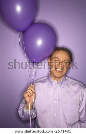 Smiling middle-aged Caucasian man on purple background holding purple balloons.