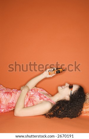 Young Caucasian woman lying on floor looking at cell phone on orange background.