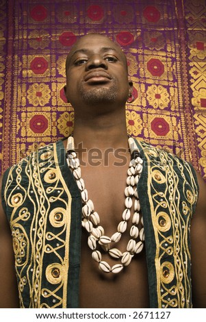 Low angle portrait of African-American mid-adult man wearing embroidered African vest and beads.