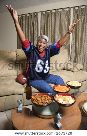 Portrait of a Middle-aged African-American woman wearing a football jersey with hands in the air watching football game.
