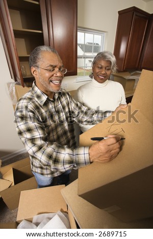 Middle-aged African-American male labeling moving box with wife in background.