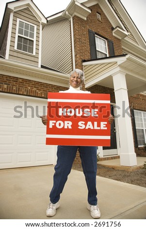 Portrait of middle-aged African-American female outside house with for sale sign.