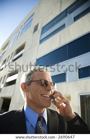 Prime adult Caucasian man in suit smiling and talking on cellphone in urban setting.