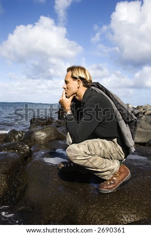 Caucasion mid-adult man kneeling on rocky coast looking at ocean in Maui, Hawaii.