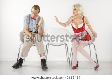 Caucasian young blonde woman sitting reaching over to shy Caucasian young man dressed like nerd.