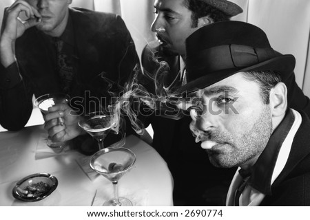 Three Caucasian prime adult males in retro suits sitting at table drinking cocktails.
