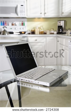 Open laptop computer on top of glass top kitchen table.