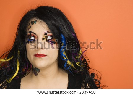 Portrait of Caucasian woman with unique makeup and hair against orange background.