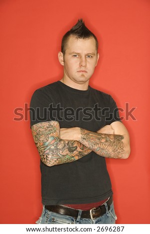 stock photo Caucasian man with mohawk and tattoos standing with arms 
