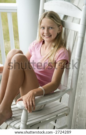 Caucasian pre-teen girl sitting in rocking chair on porch smiling.