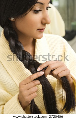 Close up profile of Asian/Indian young woman braiding hair.