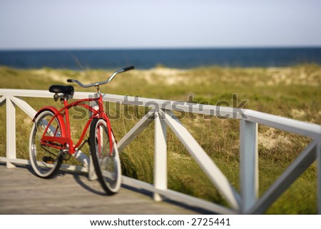 Red beach cruiser bicycle leaning against walkway rail on beach on Bald Head Island, North Carolina.