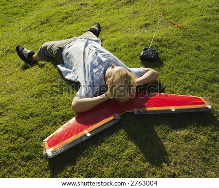 Pre-teen Caucasian male laying and resting his head on airplane and grassy knoll.