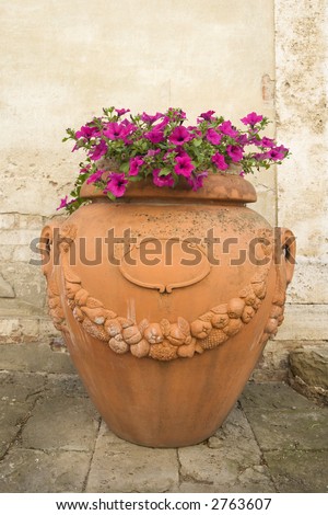Clay pot with pink petunia flowers on sidewalk in Venice, Italy.