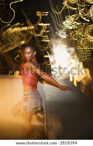 Young sexy African-American woman on patio in New York City, New York at night with blurred lights.