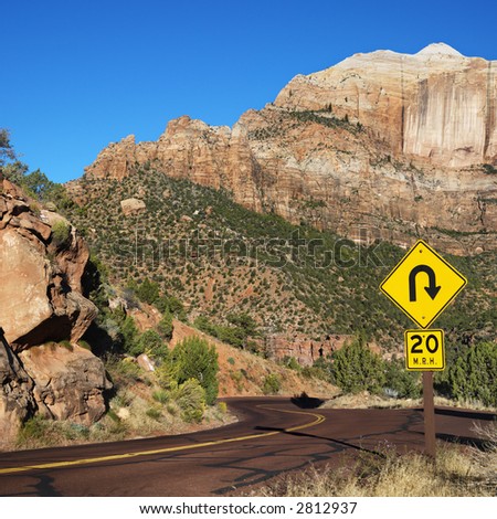 Curve caution sign on two lane road winding through rocky desert cliffs in Zion National Park, Utah.
